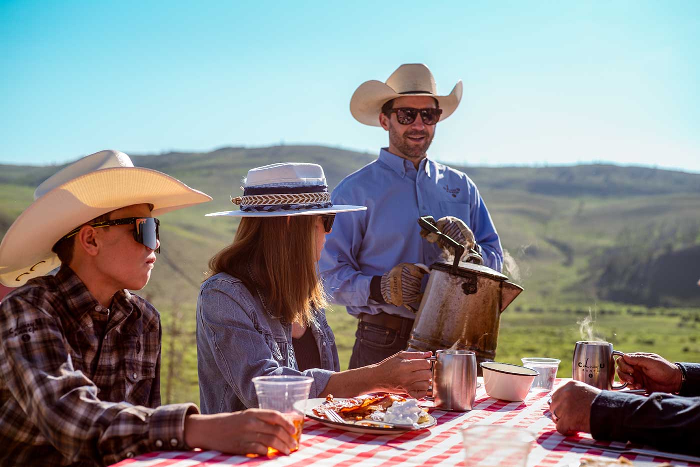 a C Lazy U staff member stands ready to serve coffee to a family sitting at a picnic table
